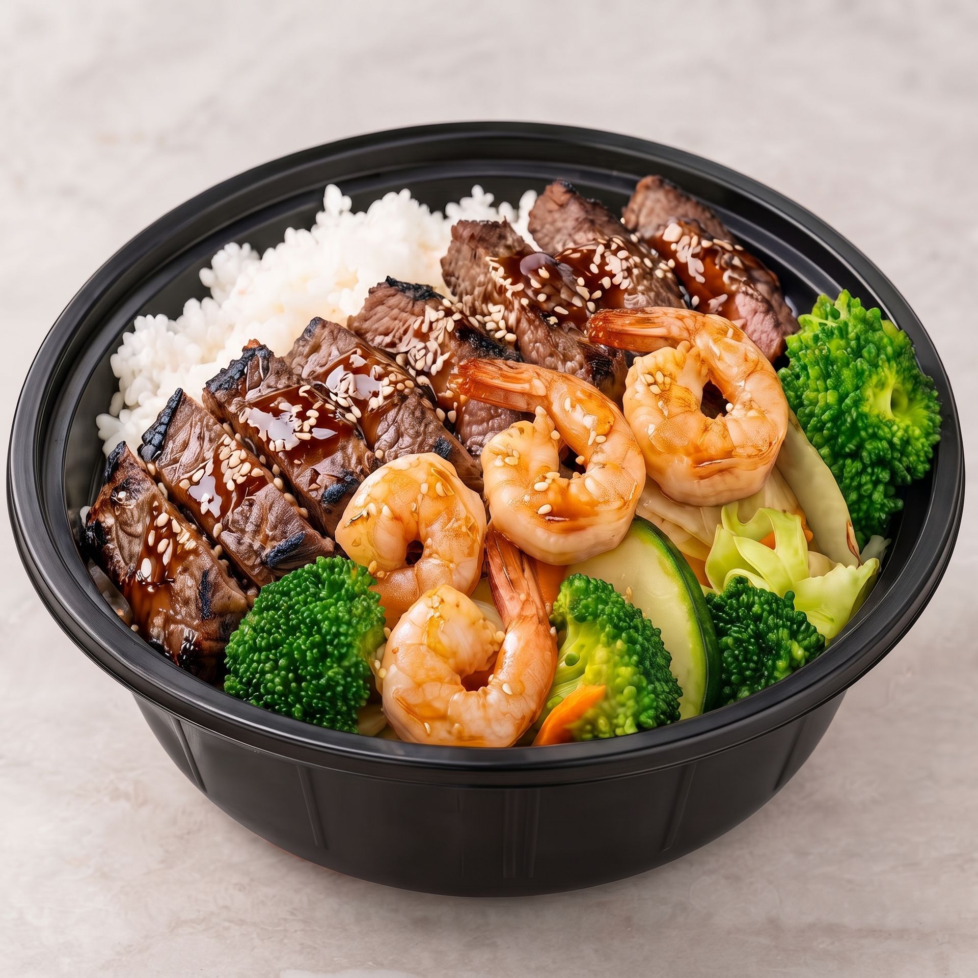 Teriyaki beef bowl with rice, shrimp, broccoli, and vegetables in a black takeout container