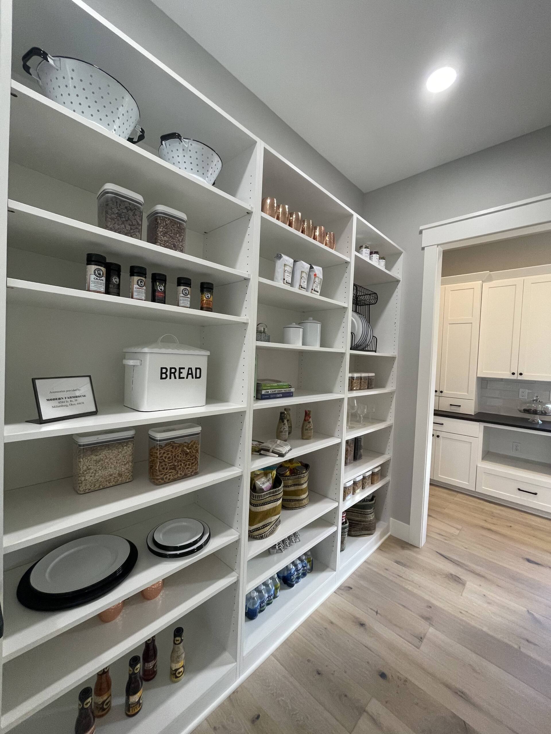 A walk-in pantry with white shelves neatly organized with dry goods, jars, a bread box, and serving dishes.
