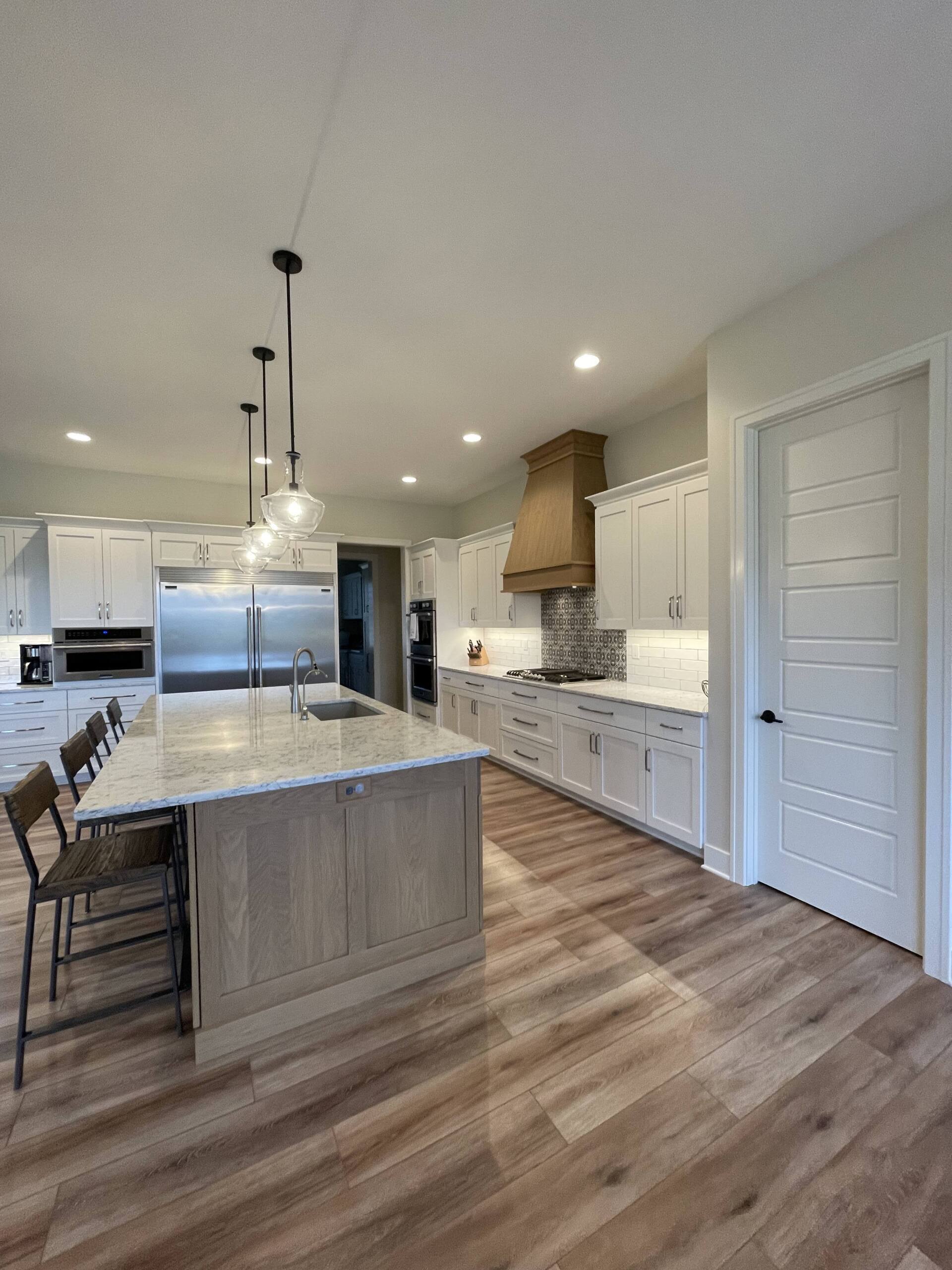 A bright kitchen with a light wood island, white cabinets, stainless steel appliances, and wood-look flooring.