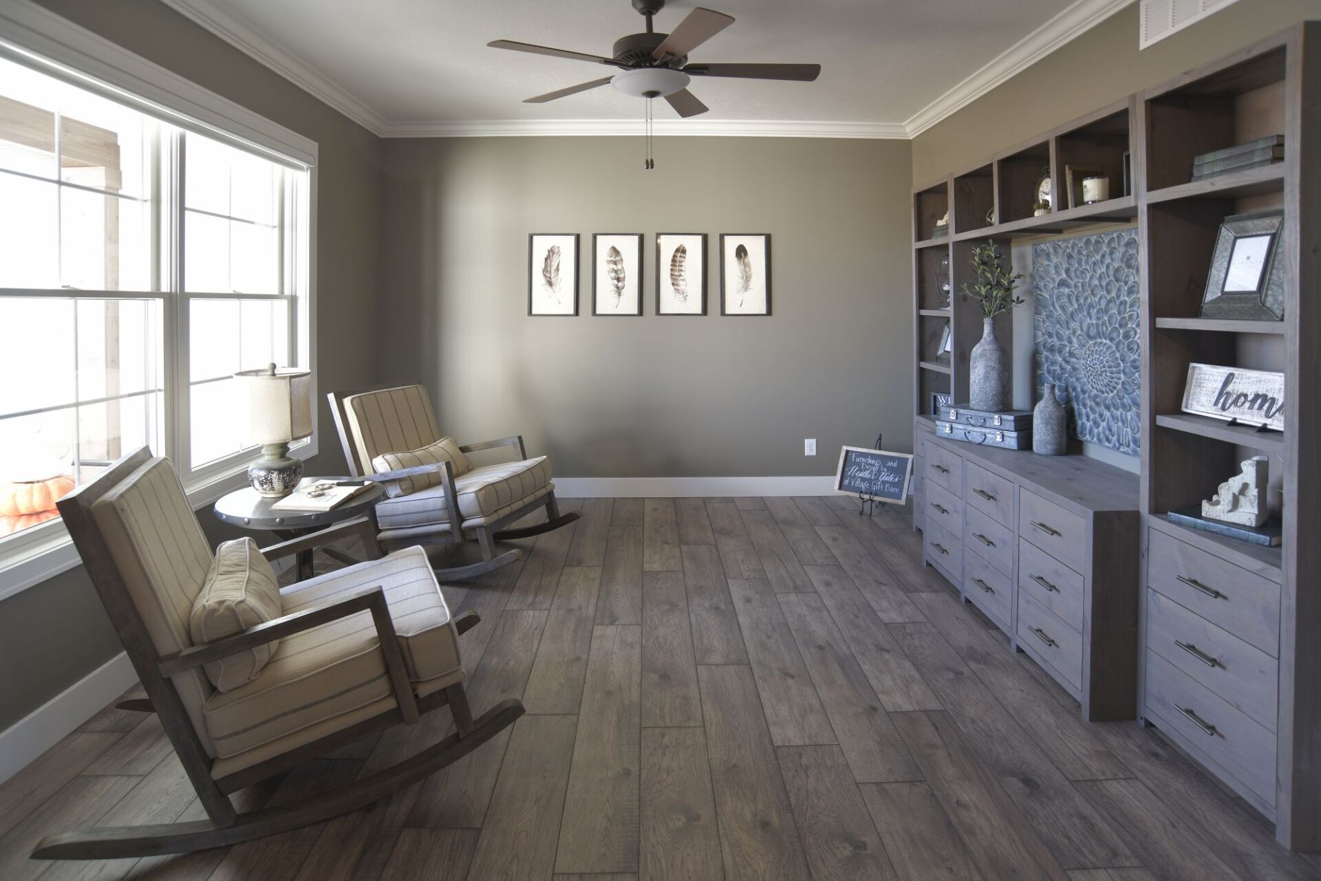 A quiet sitting area with two rocking chairs, a side table, a large wooden bookshelf, and framed wall art.