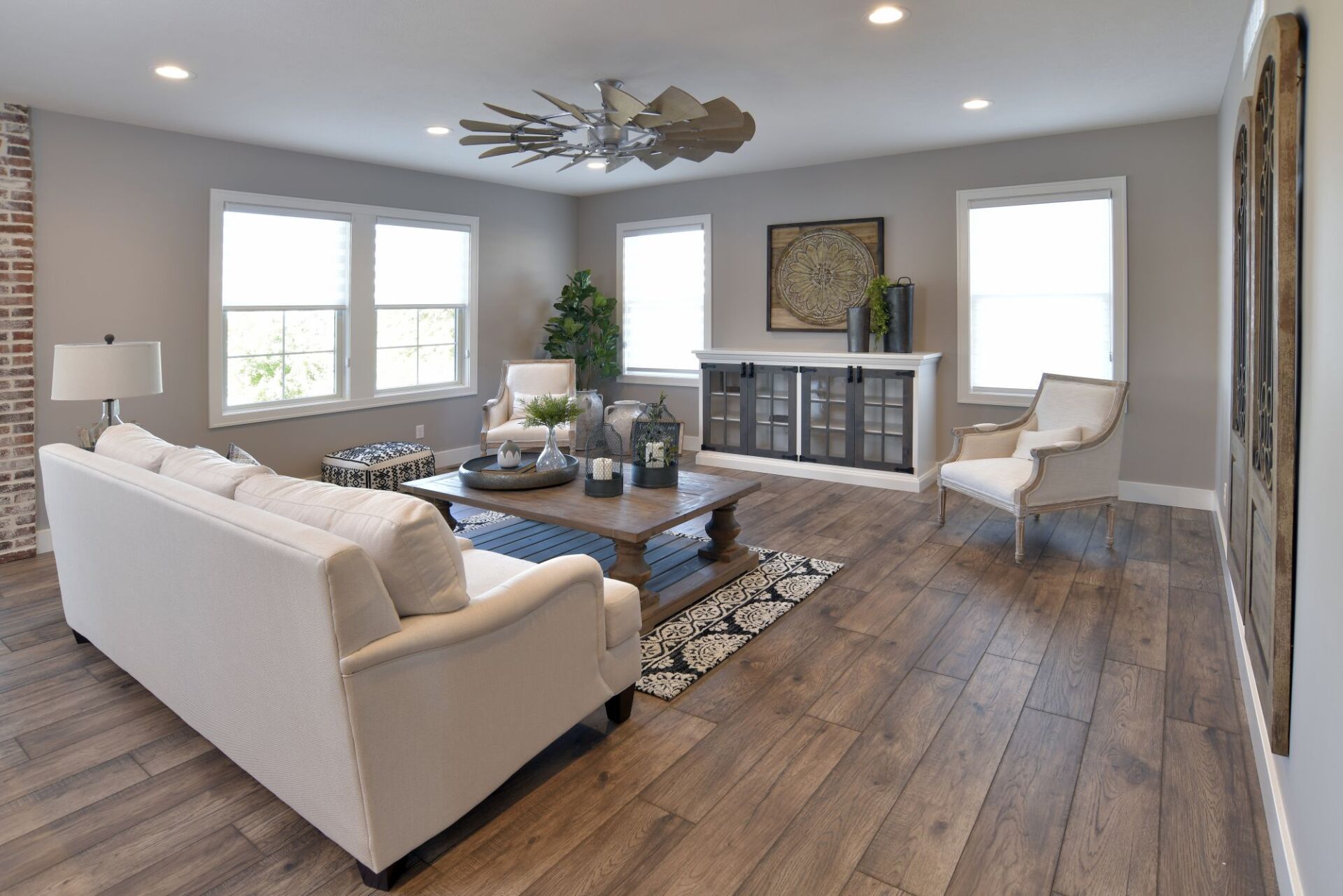 A well-lit living room with wood floors, a cream sofa, a wood coffee table, a white cabinet, and two armchairs.