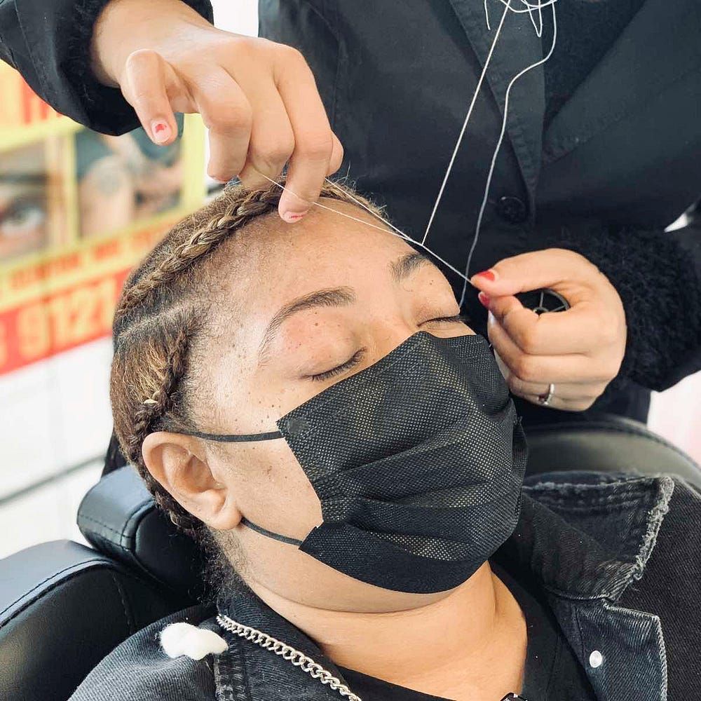 A woman wearing a black face mask is getting her eyebrows threaded.