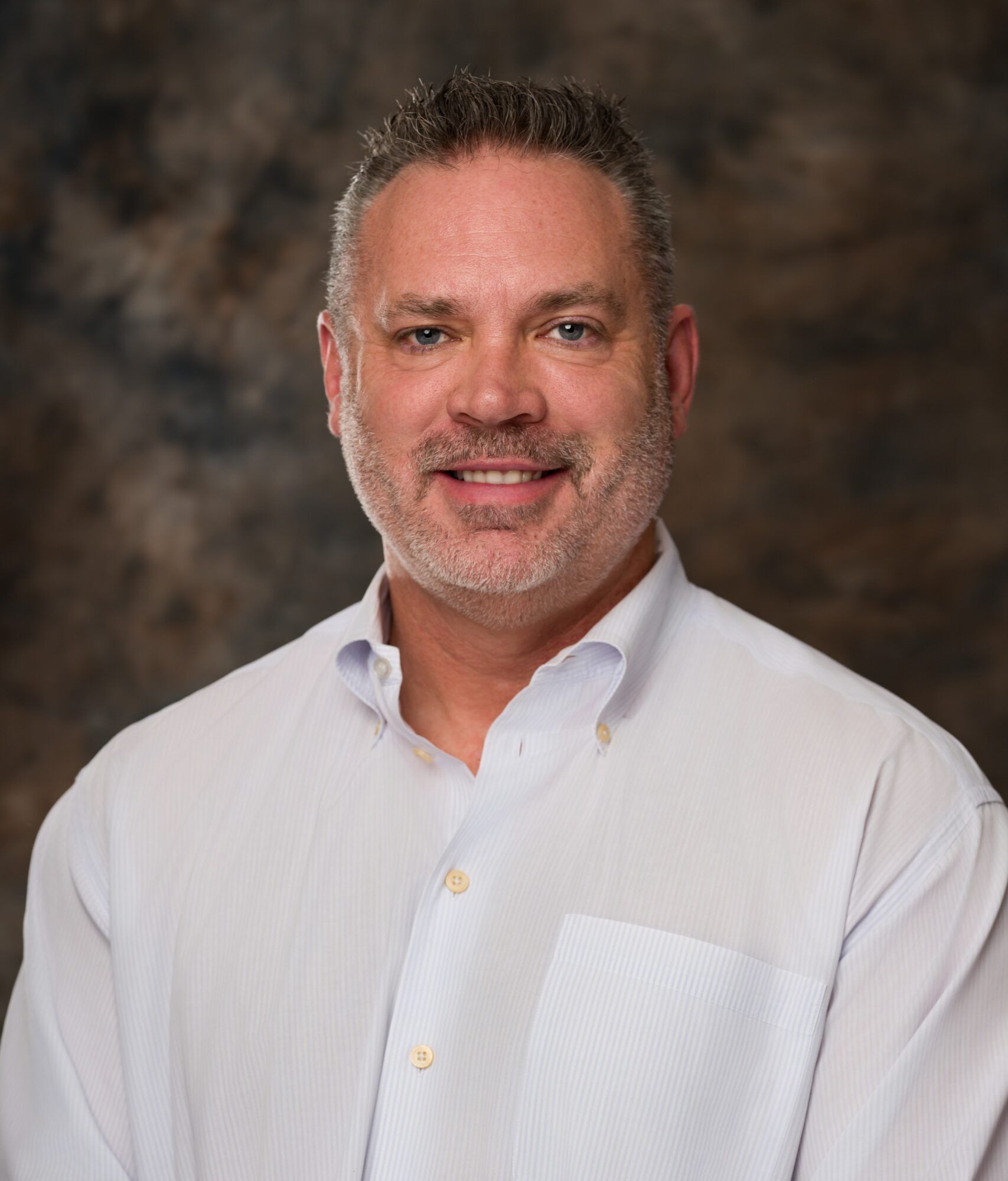 Smiling man in a white button-down shirt against a blurred studio backdrop