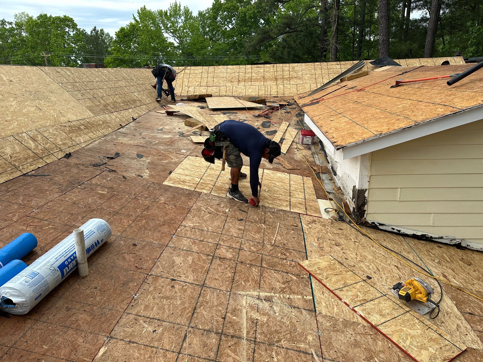 Workers replacing a roof on a house, with exposed decking and shingles in progress.