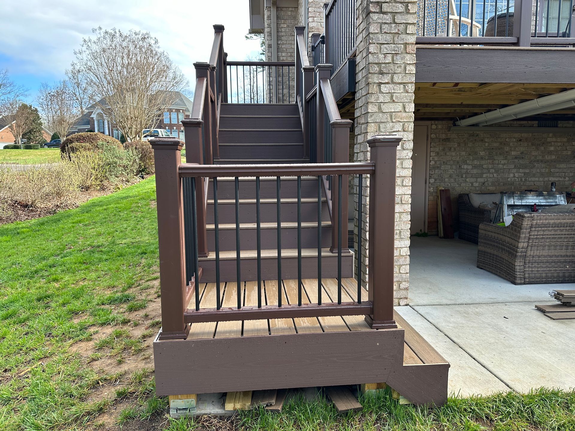 Brown wooden porch stairs with railing beside a stone house and covered patio