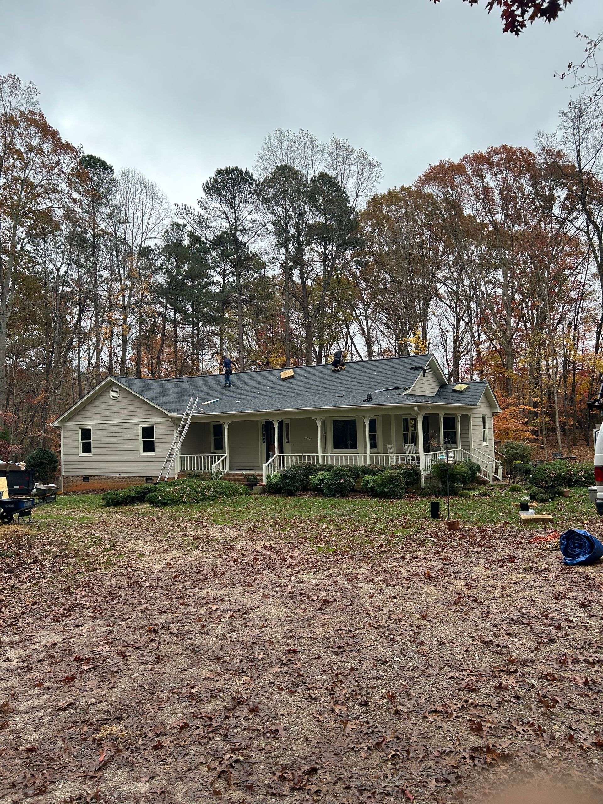 Single-story house with a gray roof and front porch, surrounded by autumn trees and a leaf-covered yard.