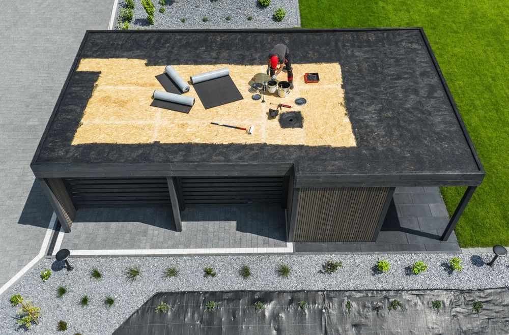Top-down view of a roof with workers installing materials on a plywood section.