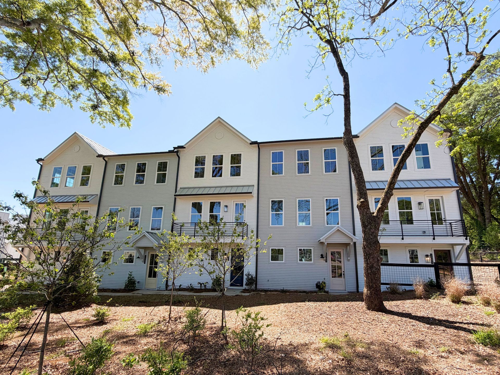 Row of pastel townhouses with porches under blooming trees on a sunny day