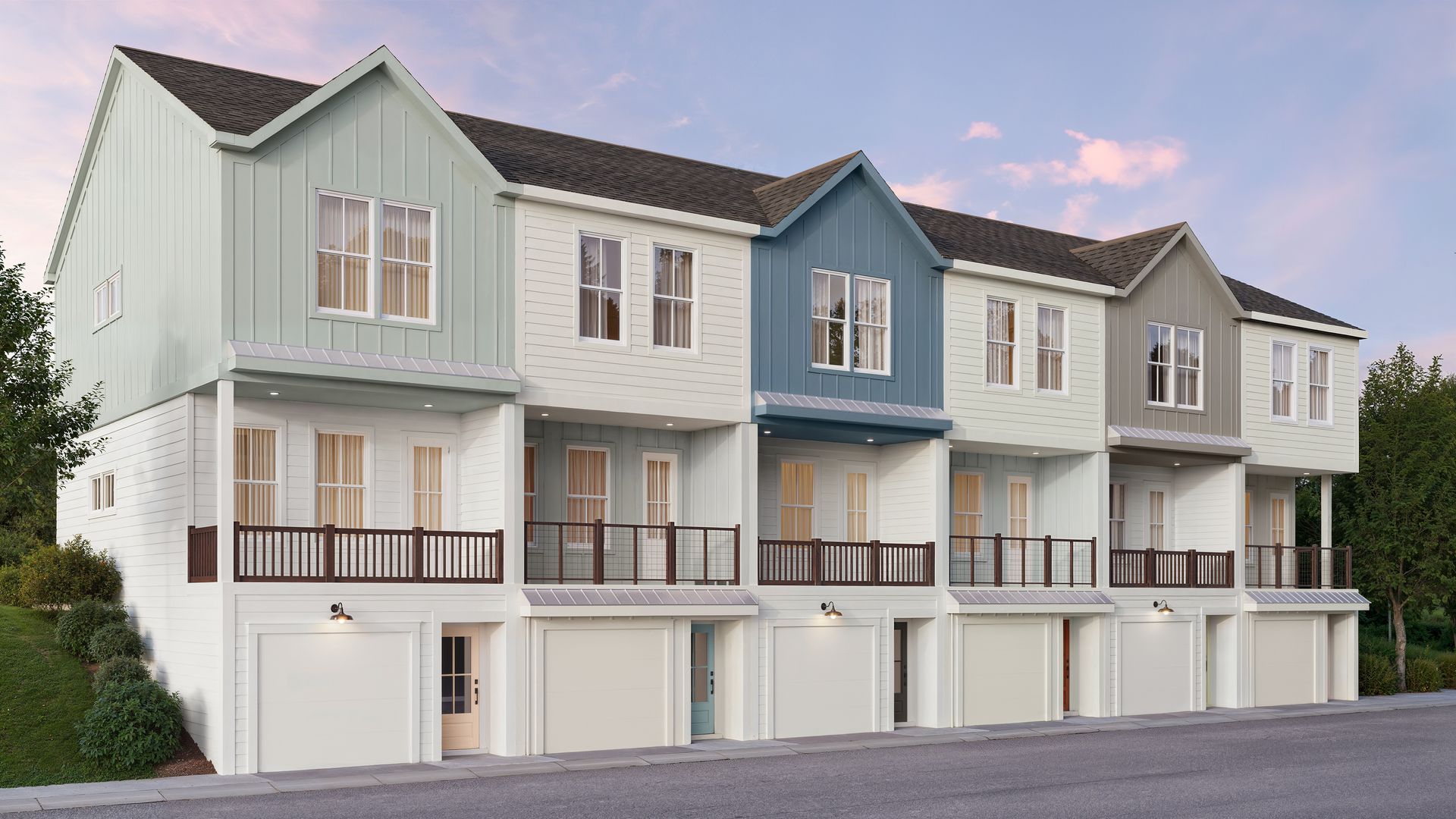 Row of pastel townhouses with attached garages and small balconies on a sloped street