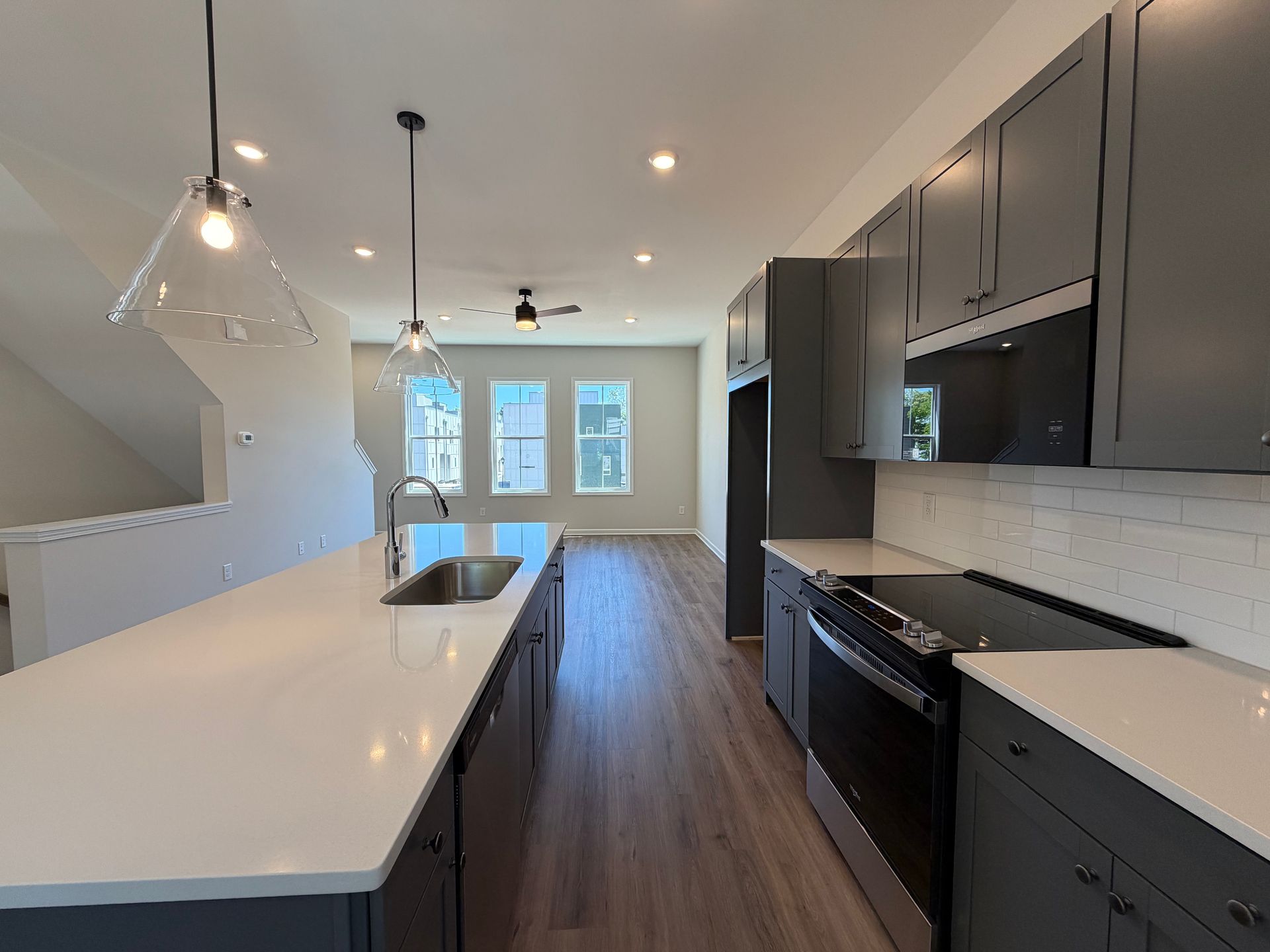 Modern kitchen with white island, dark cabinets, black countertops, and pendant lights