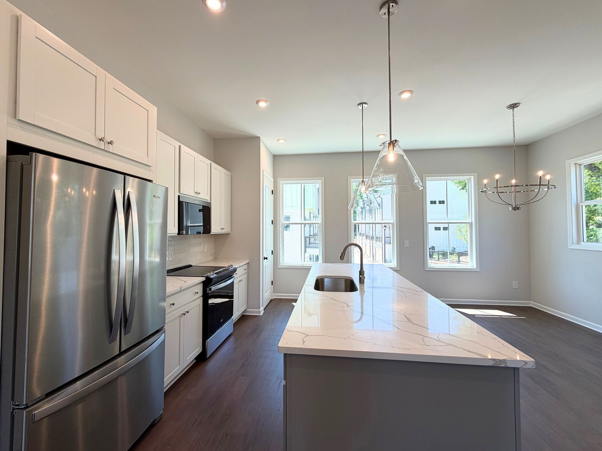 Bright modern kitchen with stainless steel appliances, white cabinets, and a large island with pendant lights.
