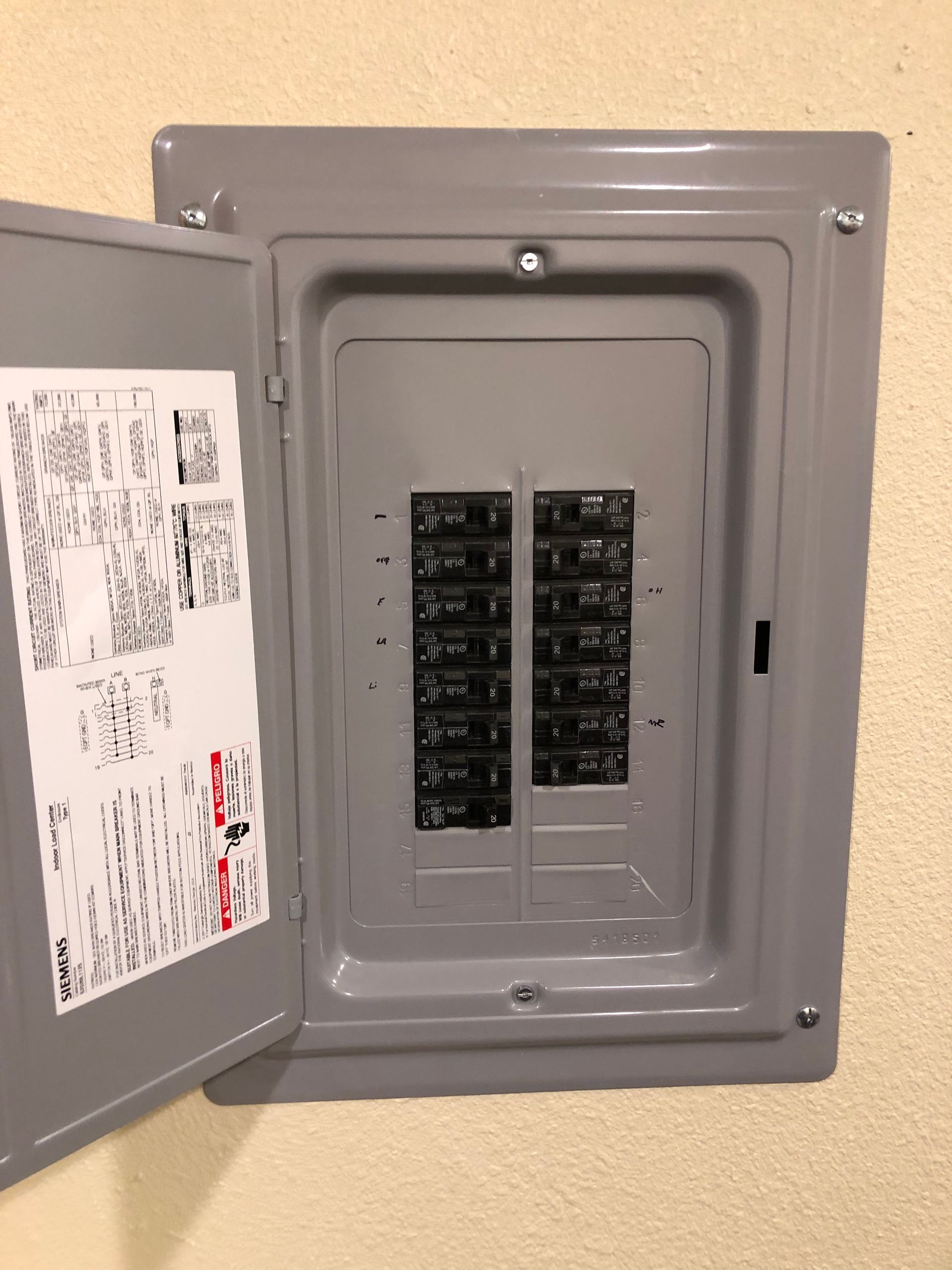 Open electrical breaker panel with gray door on a beige wall, showing multiple circuit switches.