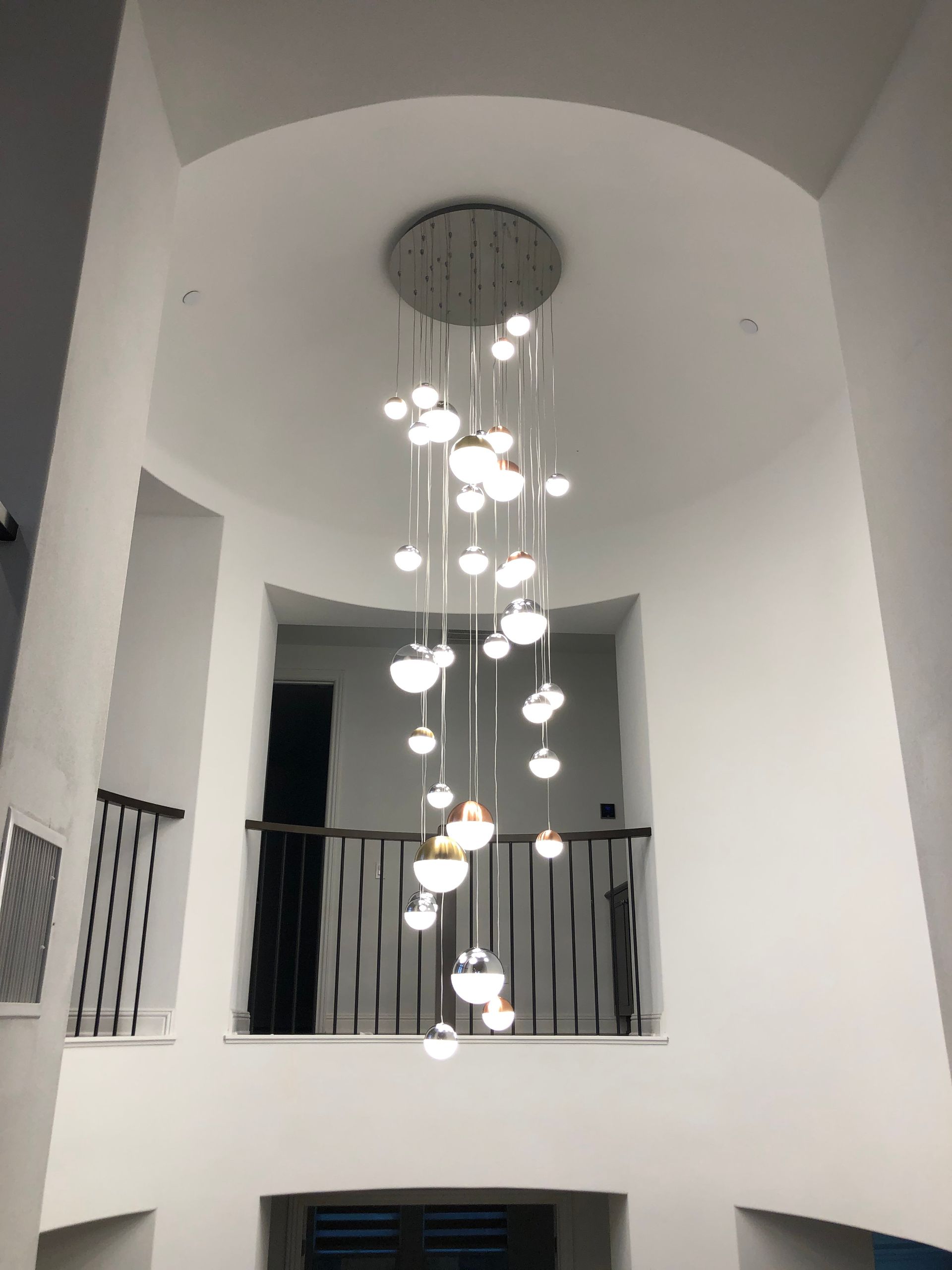 Modern white interior atrium with a hanging cluster chandelier and black balcony railings