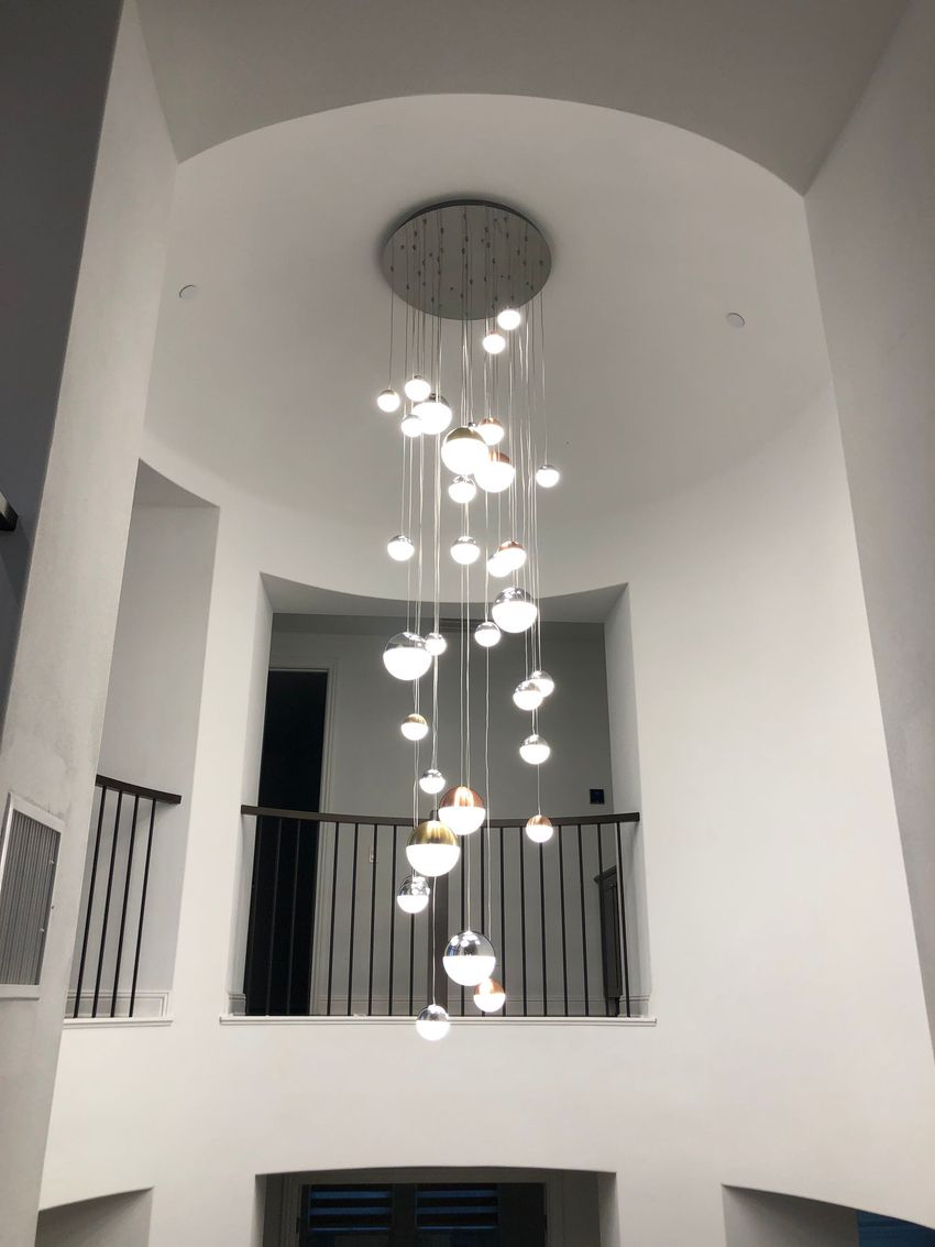 Modern atrium interior with a tall hanging chandelier and upper balcony railing