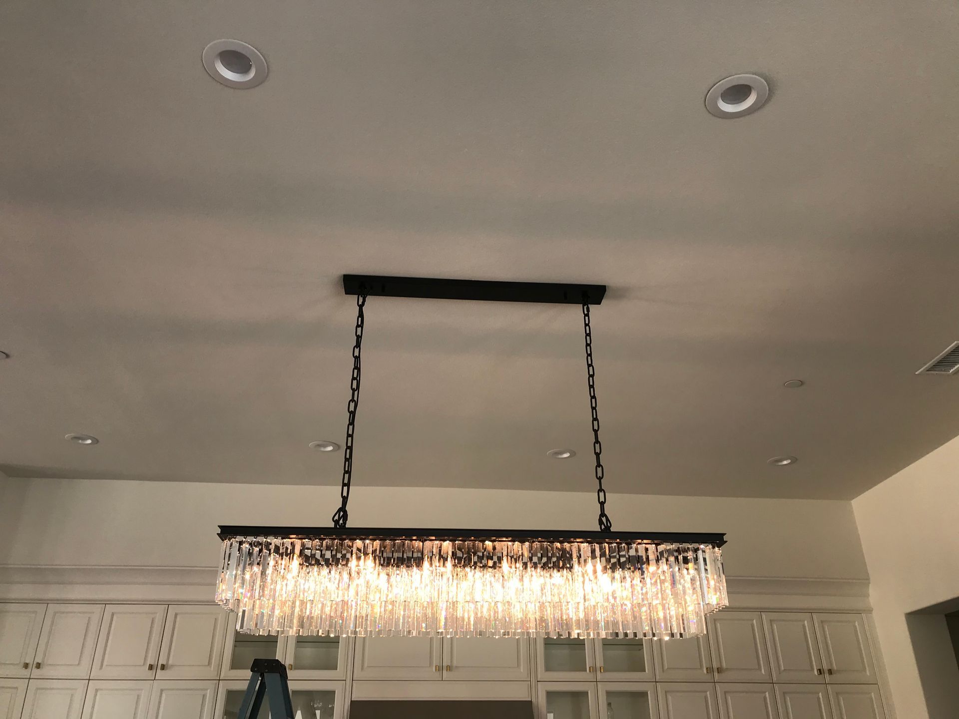Modern kitchen ceiling with a hanging crystal chandelier and recessed lights