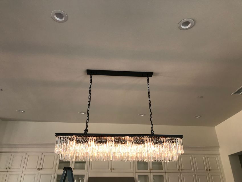 Modern kitchen with white cabinets and a hanging crystal chandelier under a gray ceiling