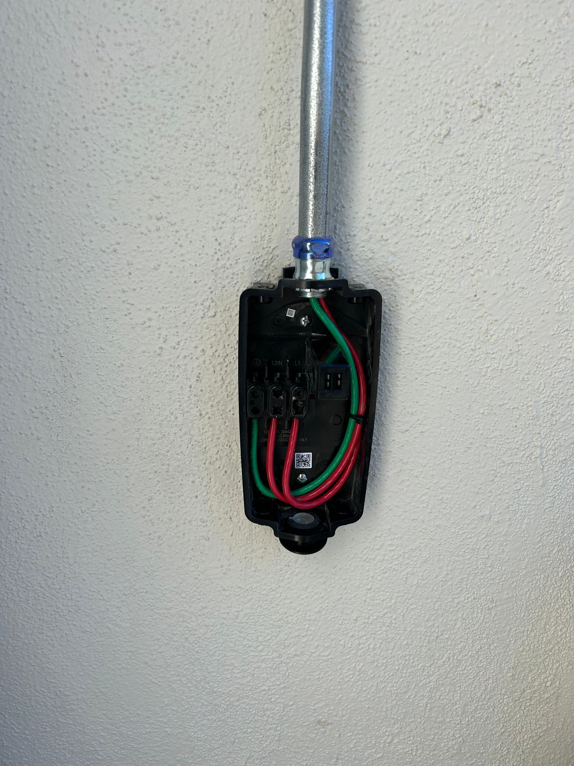 Open electrical box with red and green wires on a wall, connected to a metal conduit above.