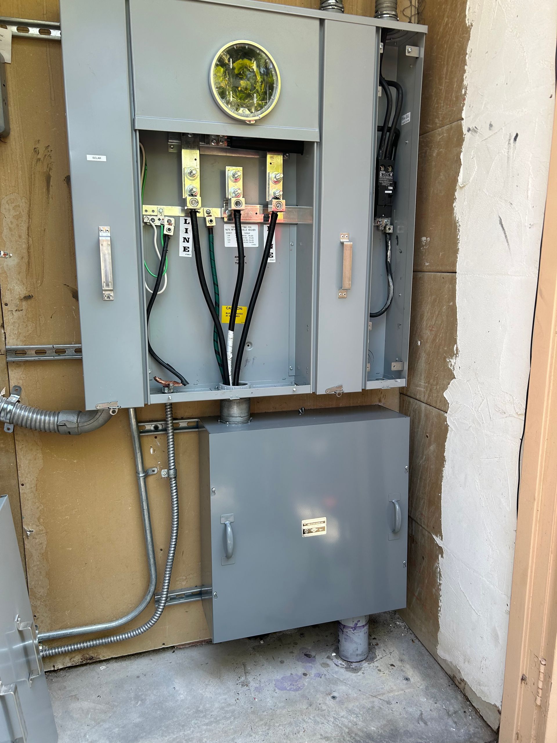 Open electrical utility panel with exposed wiring and gray boxes on a stucco exterior wall.