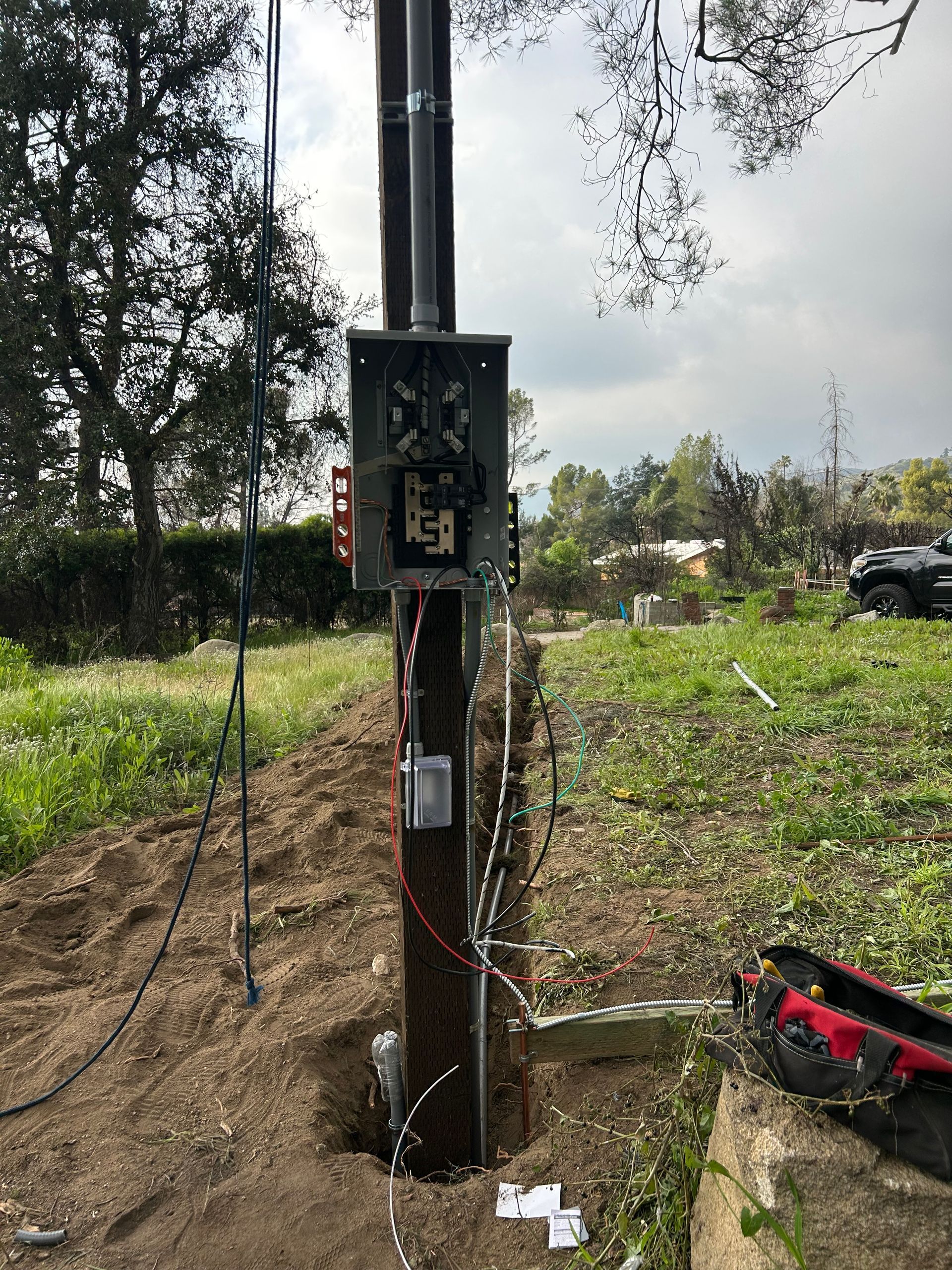 Open electrical meter and wiring on a utility pole in a grassy yard.
