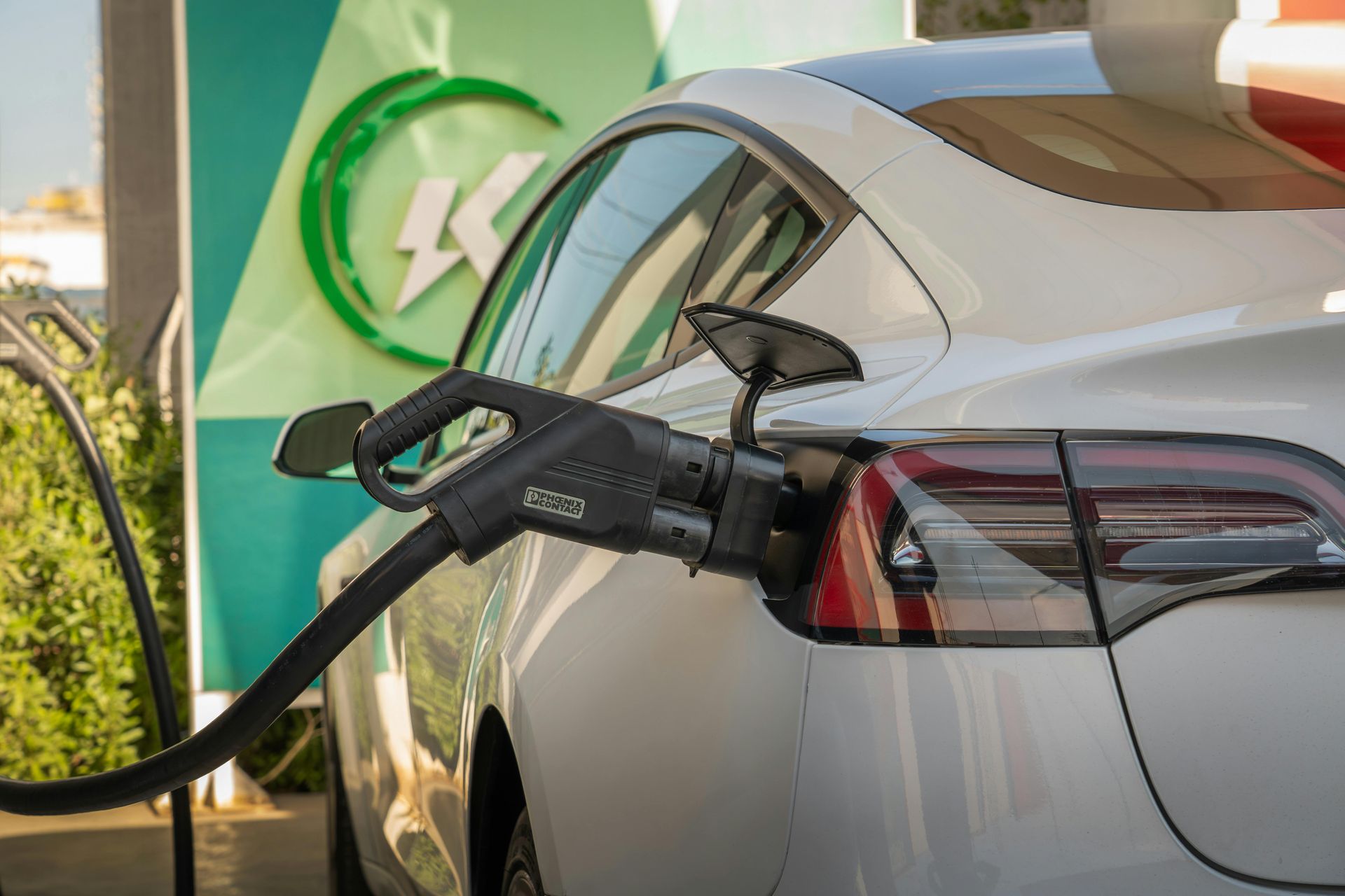 White electric car charging at a green charging station