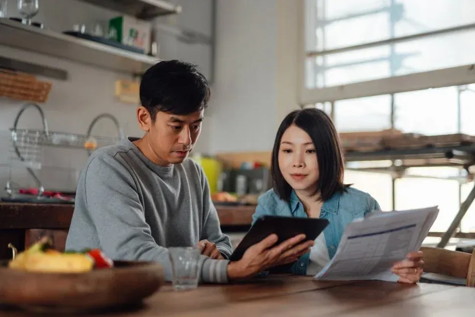 Two people reviewing documents and a tablet at a table in a bright kitchen
