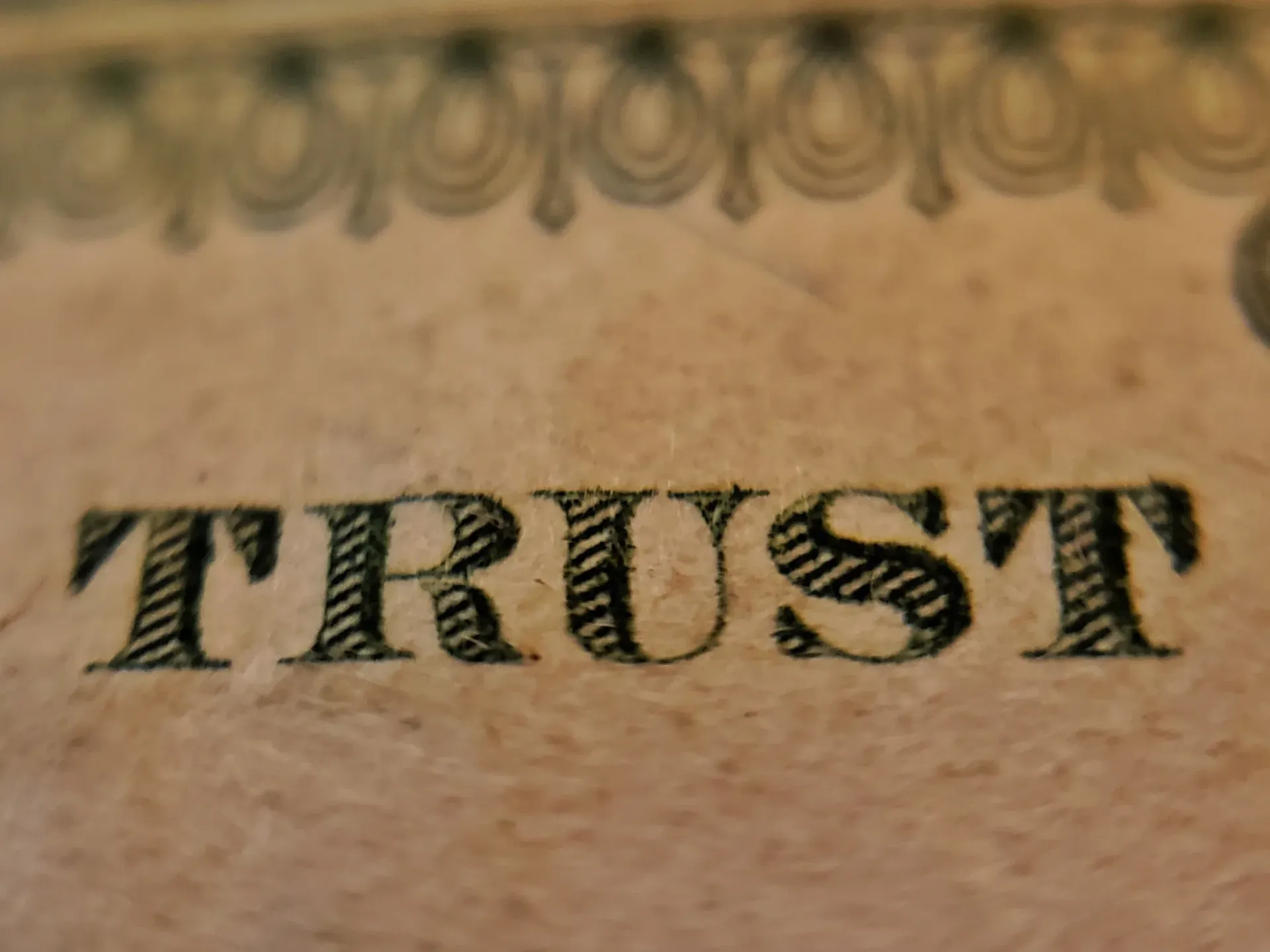 Word “TRUST” printed in black on beige paper with decorative border above.