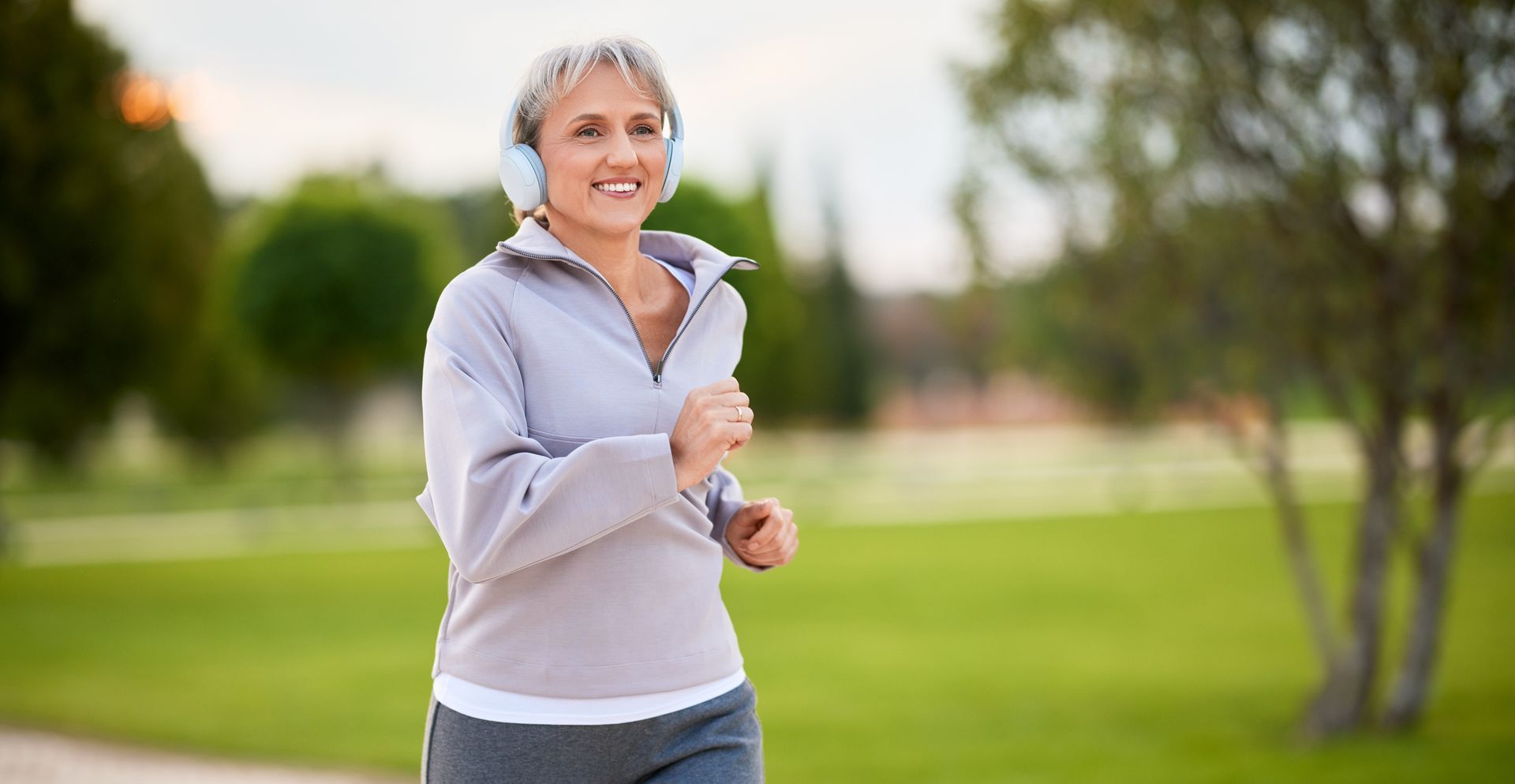 Smiling woman jogging in a park with green grass and trees in the background