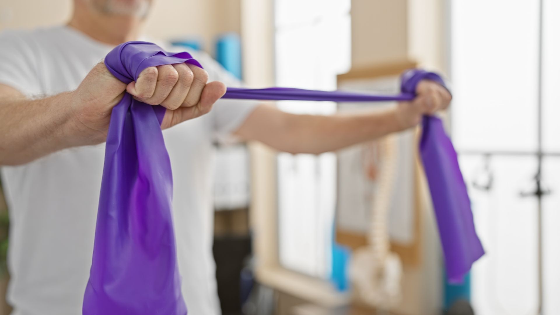 Hands stretching a purple resistance band in a bright exercise room