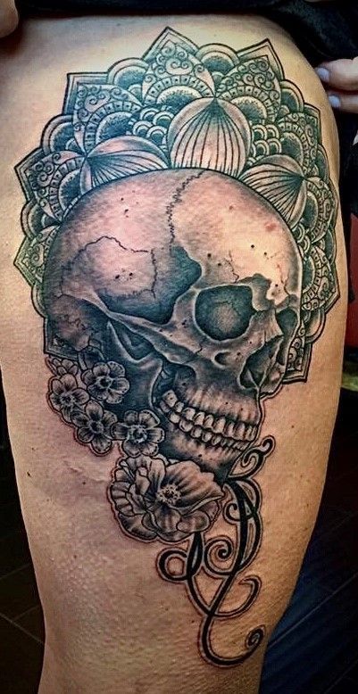 A black and white tattoo of a skull with flowers around it on a person 's leg.