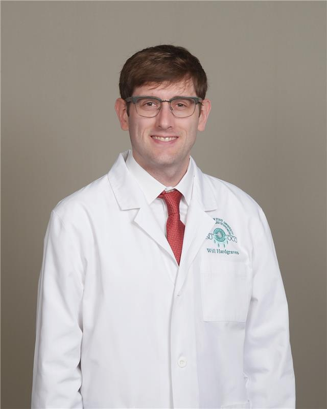 Man in white coat and glasses smiles, red tie.