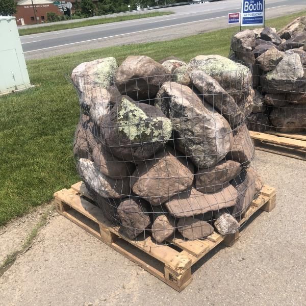 Stack of large decorative rocks in wire mesh on a wooden pallet outdoors by a roadside.