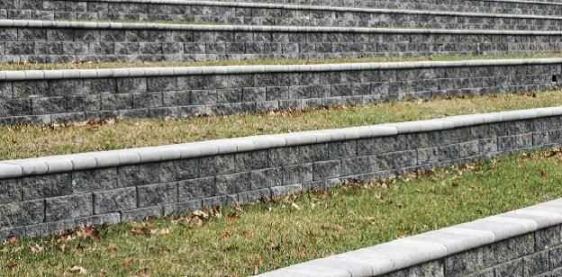 Stepped stone retaining walls with grass slopes and a paved edge in the foreground