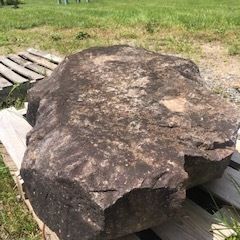 Large dark brown rock resting on a wooden pallet outdoors in a grassy area.