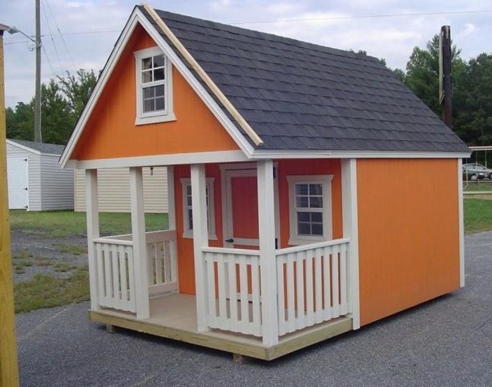 Small orange playhouse with white trim and porch on a gravel lot