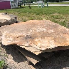 Large flat sandstone slab resting on wooden supports in a grassy outdoor area