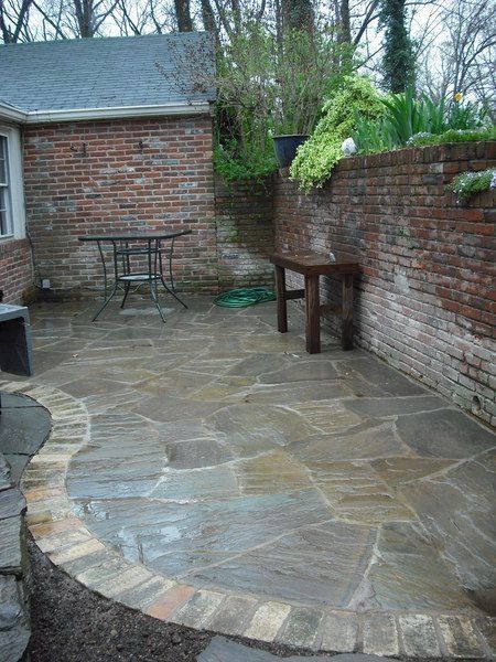 Stone patio in a brick-walled backyard with a small table, chairs, and a bench.