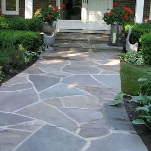 Stone walkway leading to a front porch, flanked by potted flowers and garden greenery