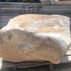 Large tan boulder on a wooden pallet, outdoors in front of stacked stone steps