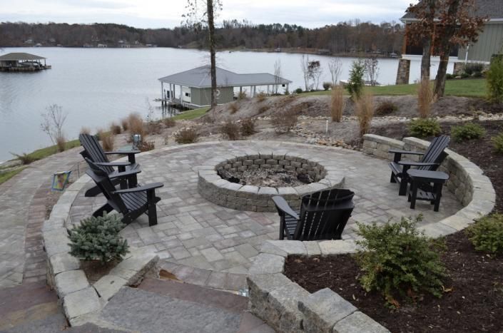Stone fire pit seating area overlooking a lake, with black chairs and a gazebo in the background