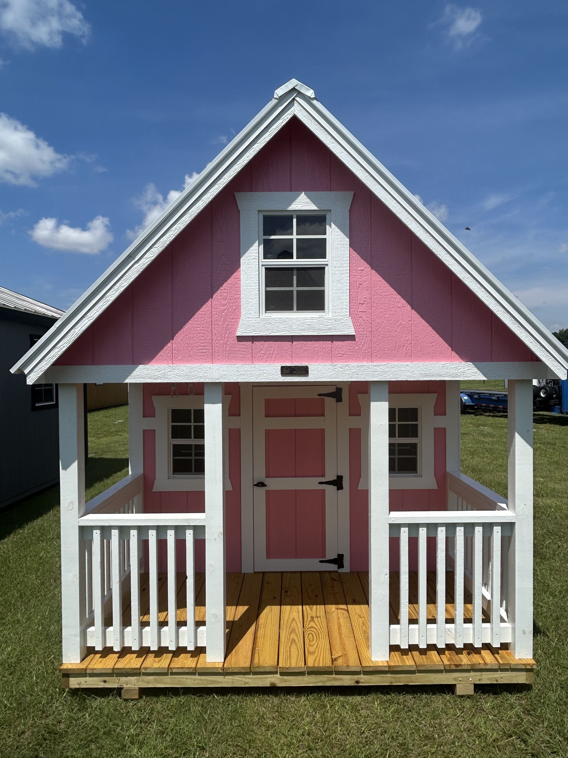 Small pink-and-white cottage with a front porch and gabled roof under a blue sky.