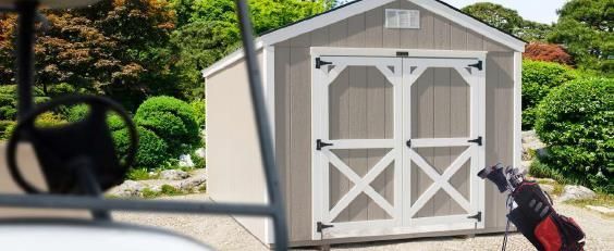 White garden shed with double doors beside a black lamppost in a landscaped yard, seen from a car window
