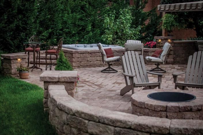 Stone patio with fire pit and outdoor dining chairs in a landscaped backyard
