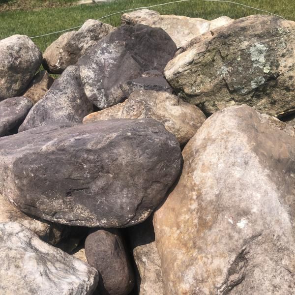 Pile of large gray and tan rocks stacked outdoors on grass