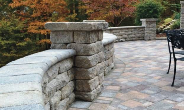 Stone patio with curved low wall and brick pillars beside autumn trees