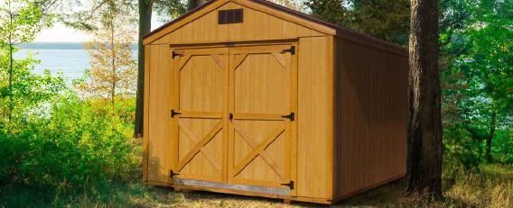 Yellow wooden shed with double doors beside a large tree in a green wooded yard