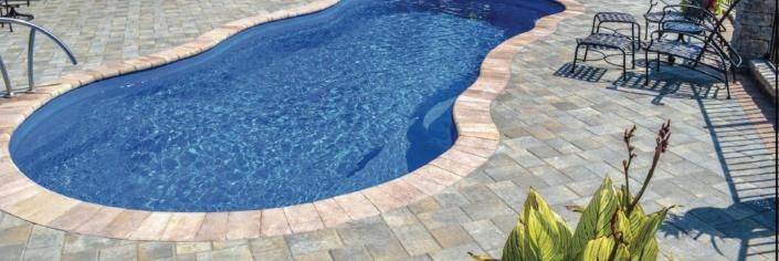Blue swimming pool with stone deck and lounge chairs in the sun