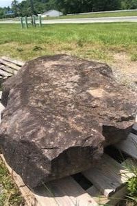 Large brown boulder resting on a wooden pallet in a grassy outdoor area.