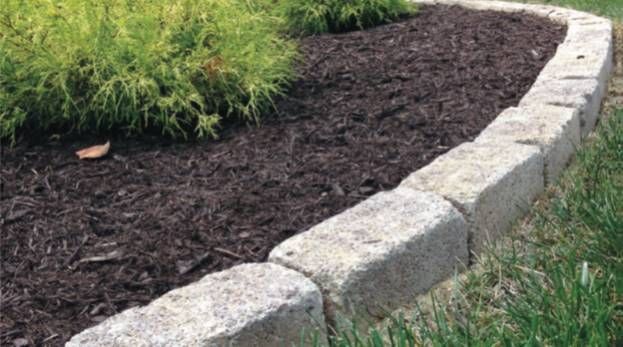Curved stone landscape border edging a mulched garden bed with green grass and plants