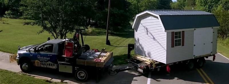 Tow truck towing a small white cabin trailer on a grassy roadside