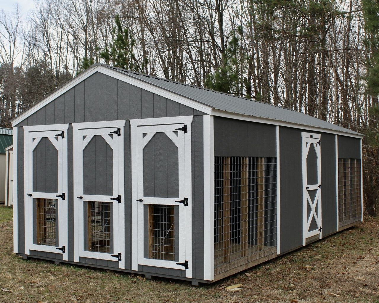 Gray-and-white wooden pet enclosure with multiple door panels, outdoors beside trees